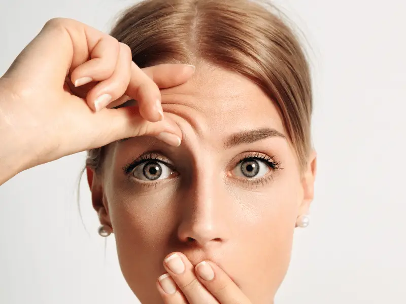 Lifting de frente y ahuecamiento de sienes: opciones que funcionan. Piel de la frente levantada a mano para previsualizar cómo un cambio en la altura de las cejas altera el ojo.