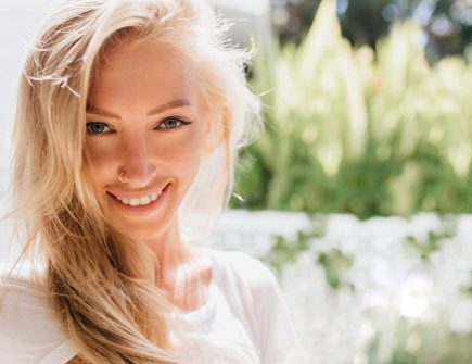 Close-up photo of smiling woman with pierced nose. Portrait of romantic blonde lady laughing and wa